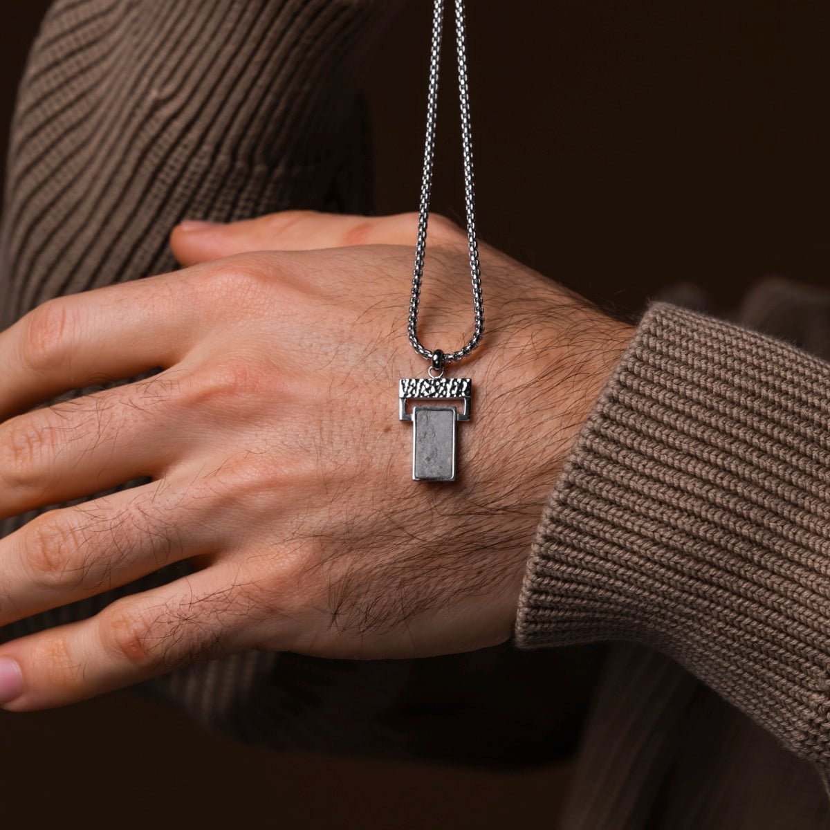 "Transcendent" necklace featuring a sleek slate and silver design, resting elegantly on a hand.