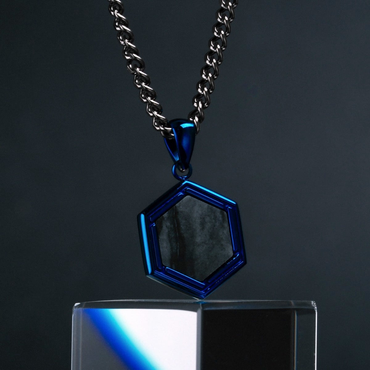 "Axis Necklace" necklace, featuring a hexagonal pendant with a metallic chain, showcases a modern design in blue and gray tones.