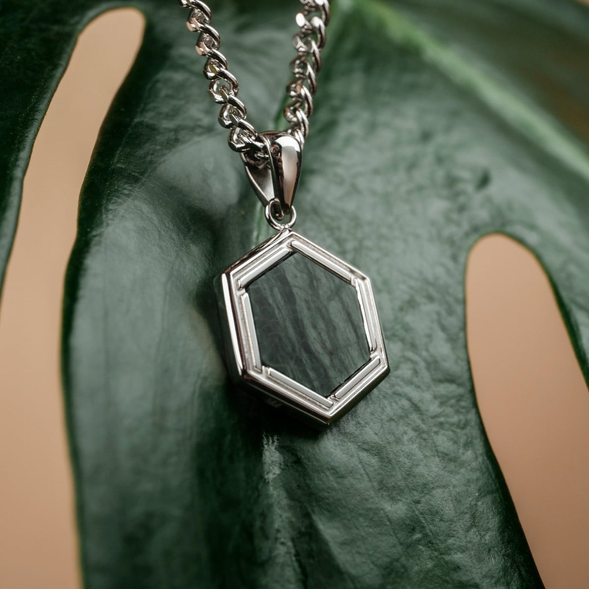 "Axis Necklace": A silver chain necklace featuring a hexagonal pendant with green marble detail.