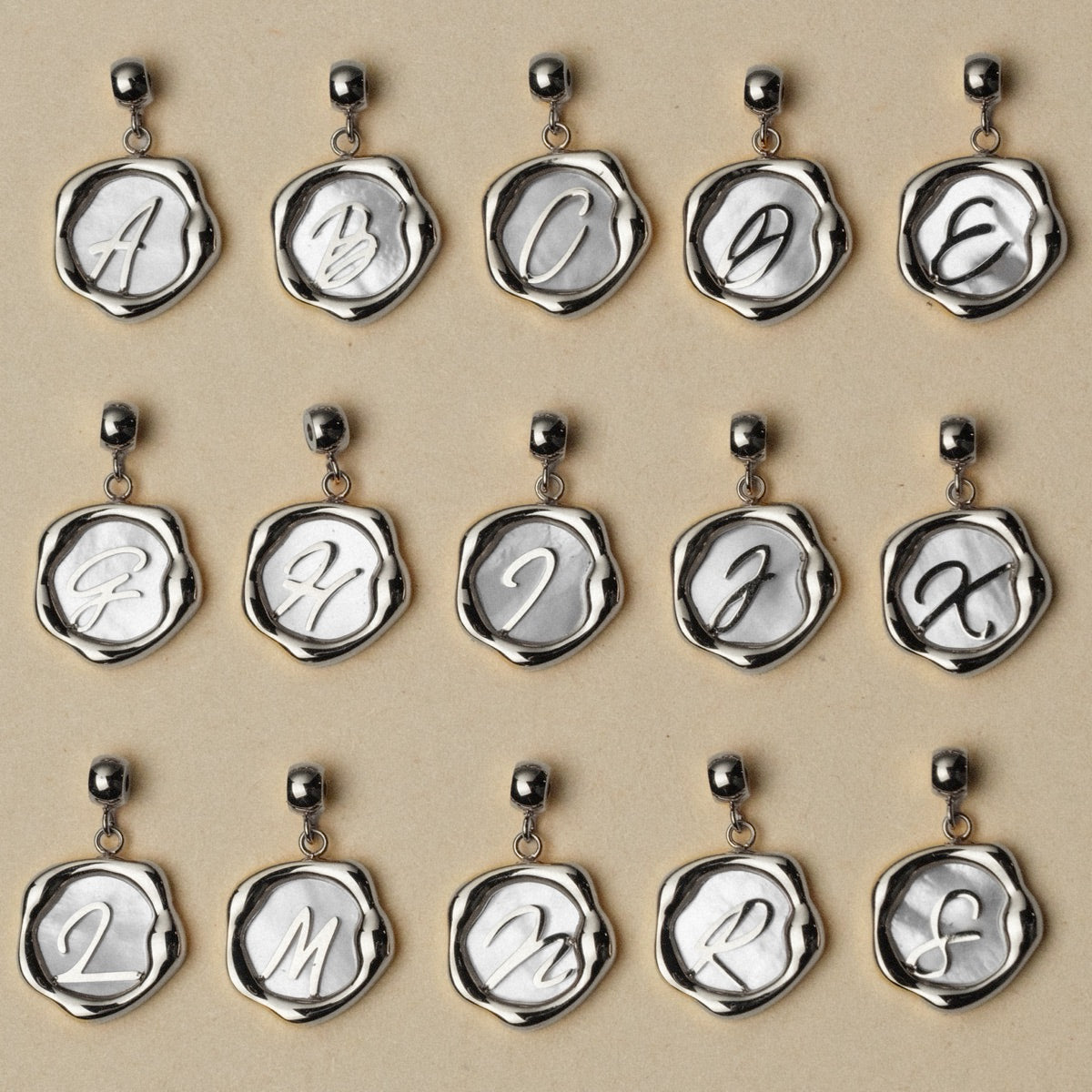 "Letter Charm A-Z" necklace charms in nacre and silver, featuring A-Z letters with an elegant and classic design.