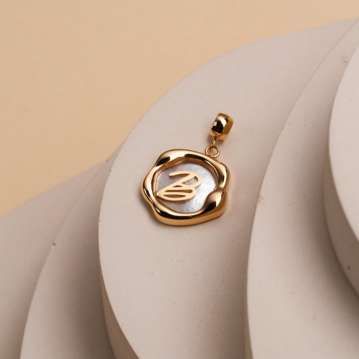 "Letter Charm A-Z": A stylish letter charm in nacre and gold with an elegant, modern design.