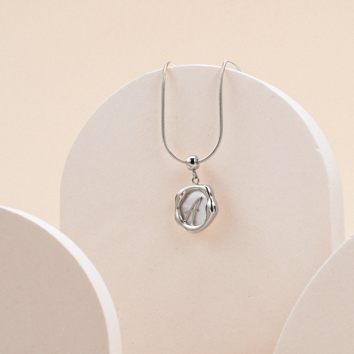 "Letter Charm A-Z" pendant with silver setting and nacre letter design, featuring a minimalist aesthetic.