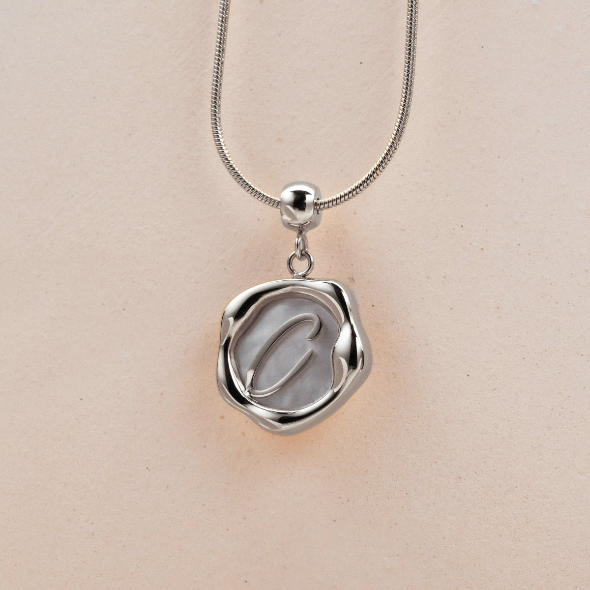 "Letter Charm A-Z" letter charm in nacre and silver, featuring an elegant circular design.