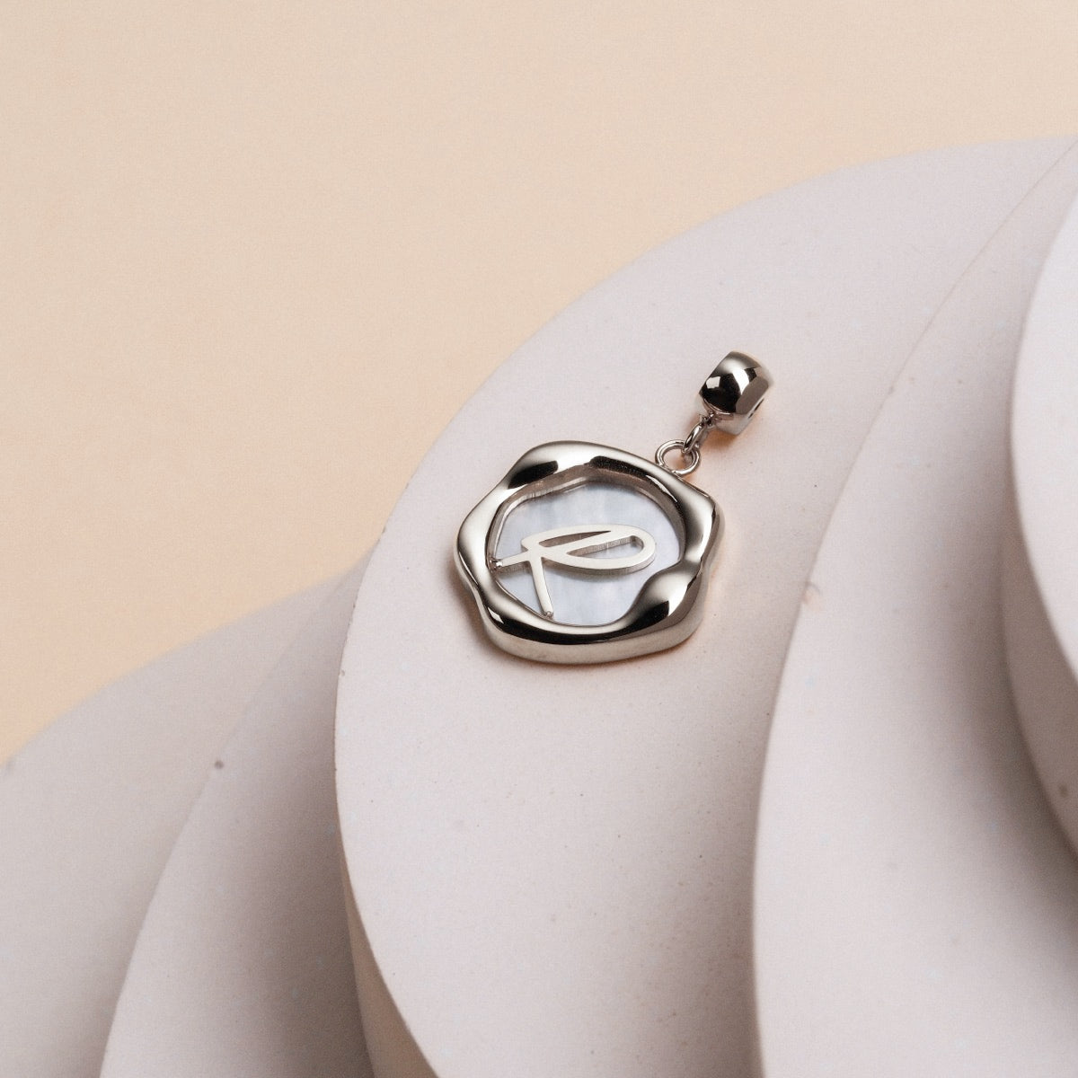 "Letter Charm A-Z", a silver and nacre letter charm with a sleek, elegant design.