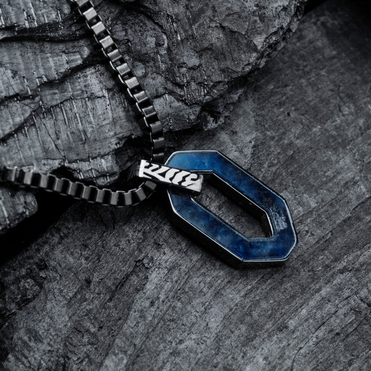 "Interplay Necklace" necklace with a geometric design in sodalite and Damascus, set against a rugged stone background.