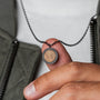 "Interplay Necklace" necklace features a circular pendant with a koa wood center and gray accents, offering a modern, earthy style.