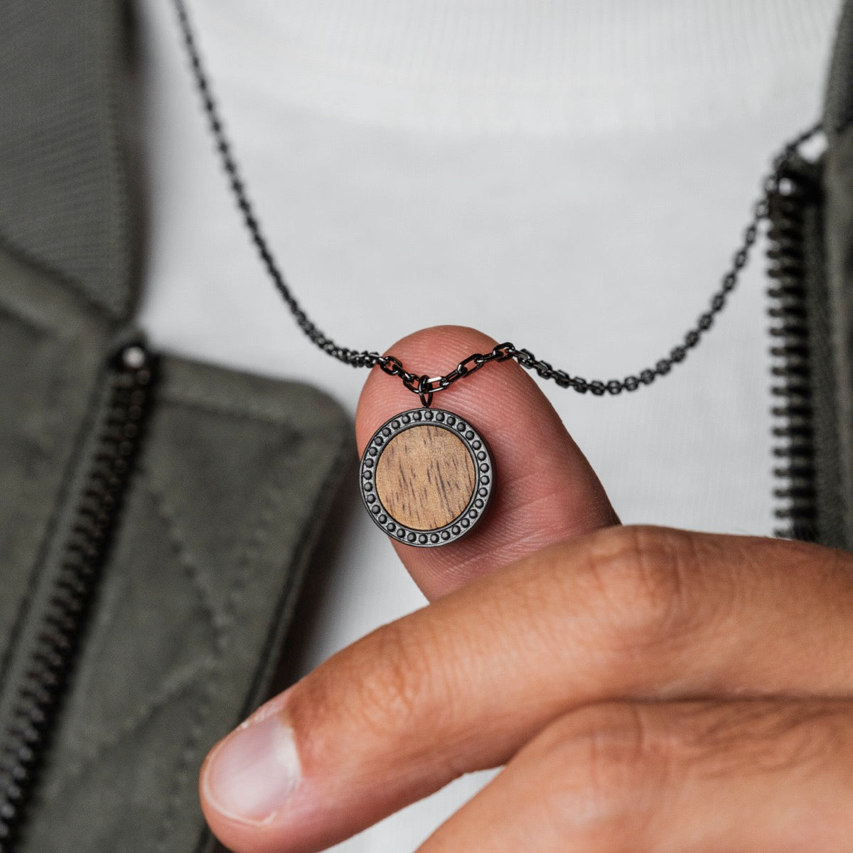 "Interplay Necklace" necklace features a circular pendant with a koa wood center and gray accents, offering a modern, earthy style.