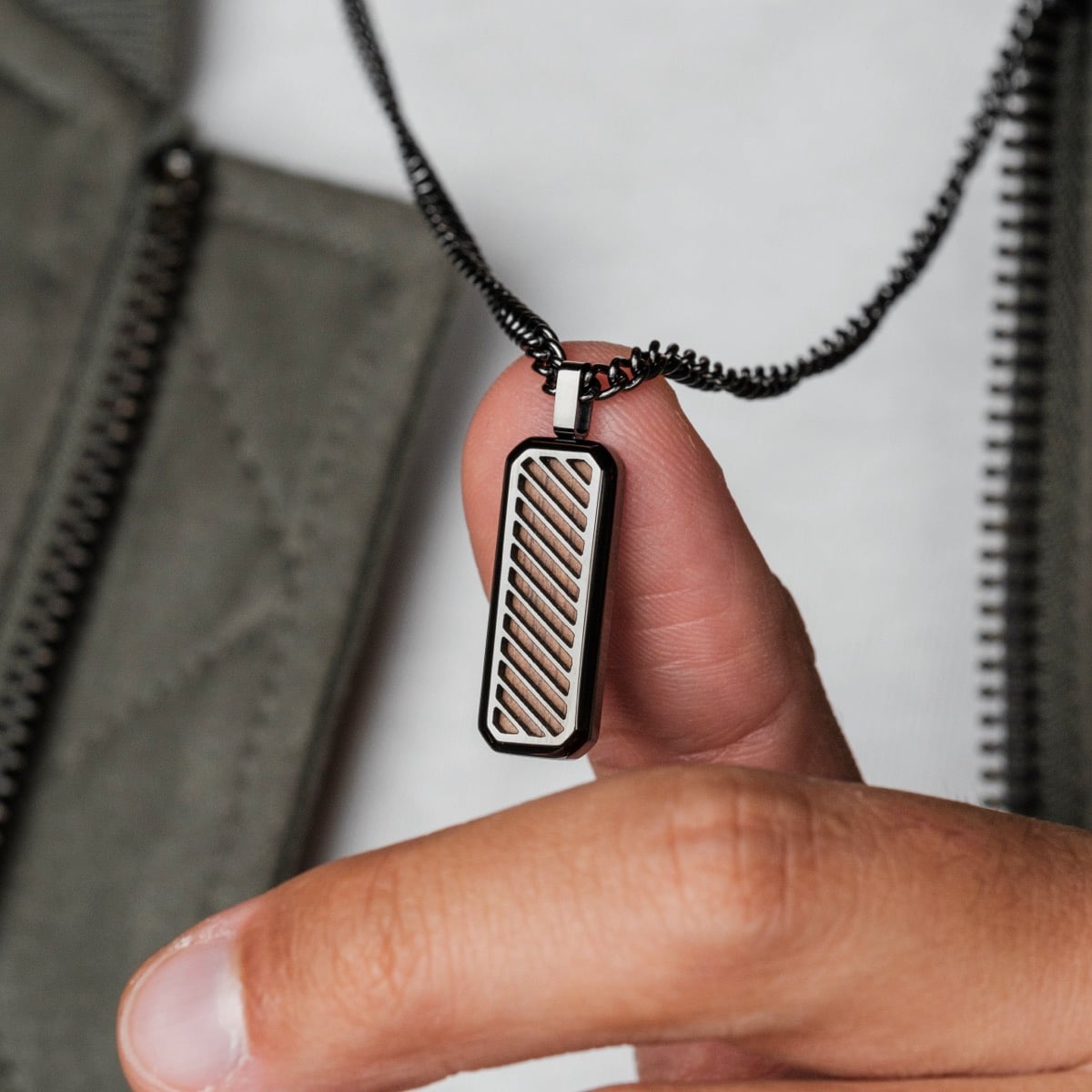 "Interplay Necklace", a modern rectangular necklace with walnut and gray accents, held by a hand.