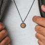 "Interplay Necklace" necklace with a koa wood pendant and gray chain, featuring a stylish circular design.