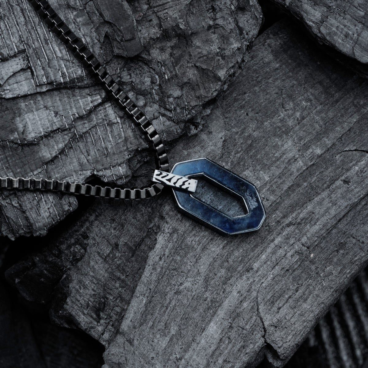 "Interplay Necklace" features a geometric necklace design with sodalite and Damascus steel accents, set against a textured backdrop.
