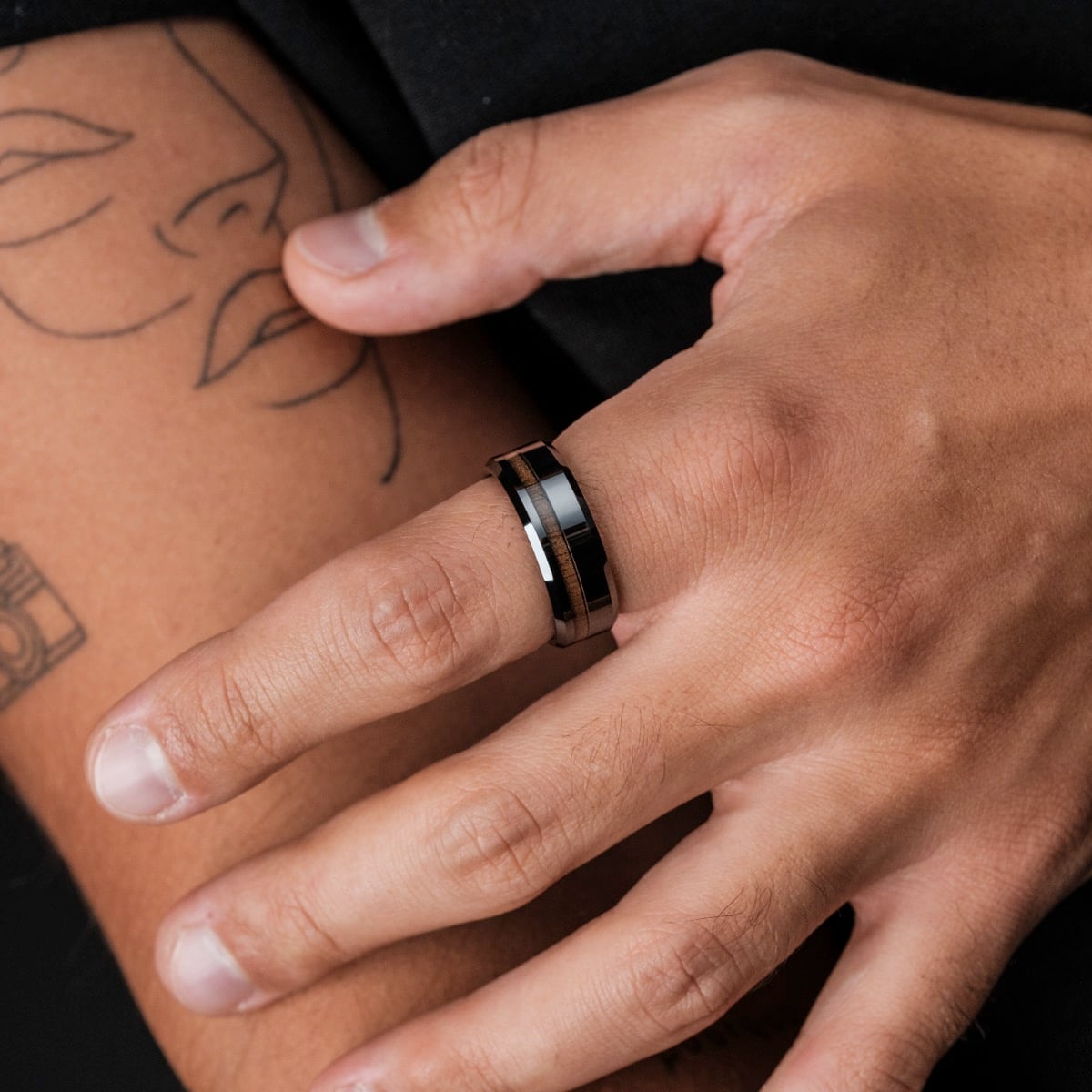 "Sumo Ring", a stylish ring made of walnut and ceramic, displayed on a hand with minimalistic tattoos.