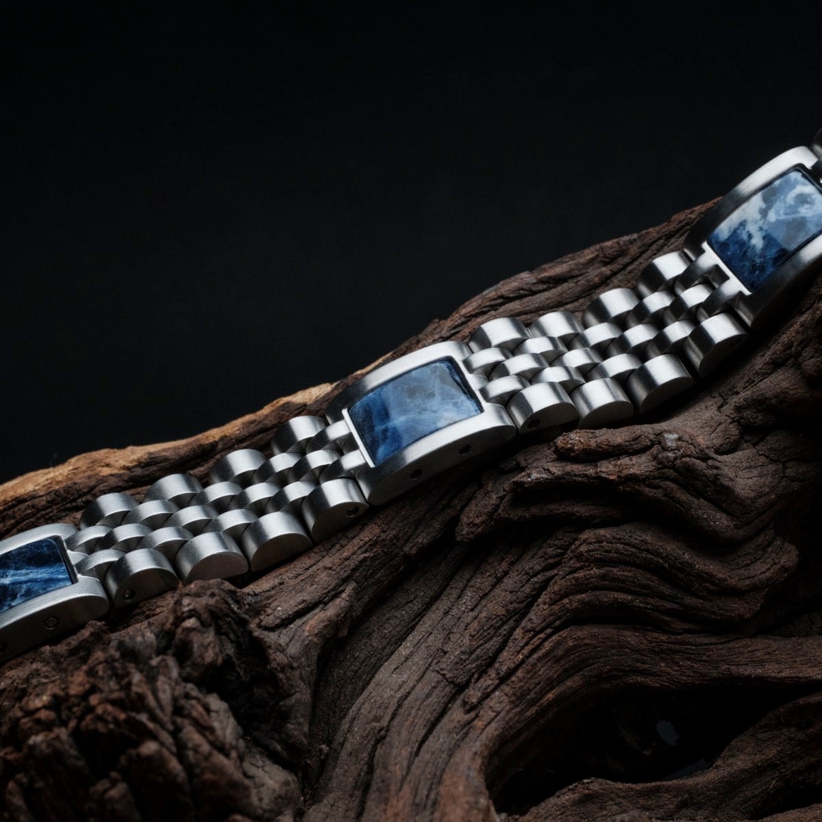 "Pentachord" bracelet in silver with a blue marble accent, showcasing a sleek and stylish design on a rustic wood background.