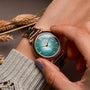 "Sunglister" wristwatch with a green mother-of-pearl face and rose gold accents worn on an arm.
