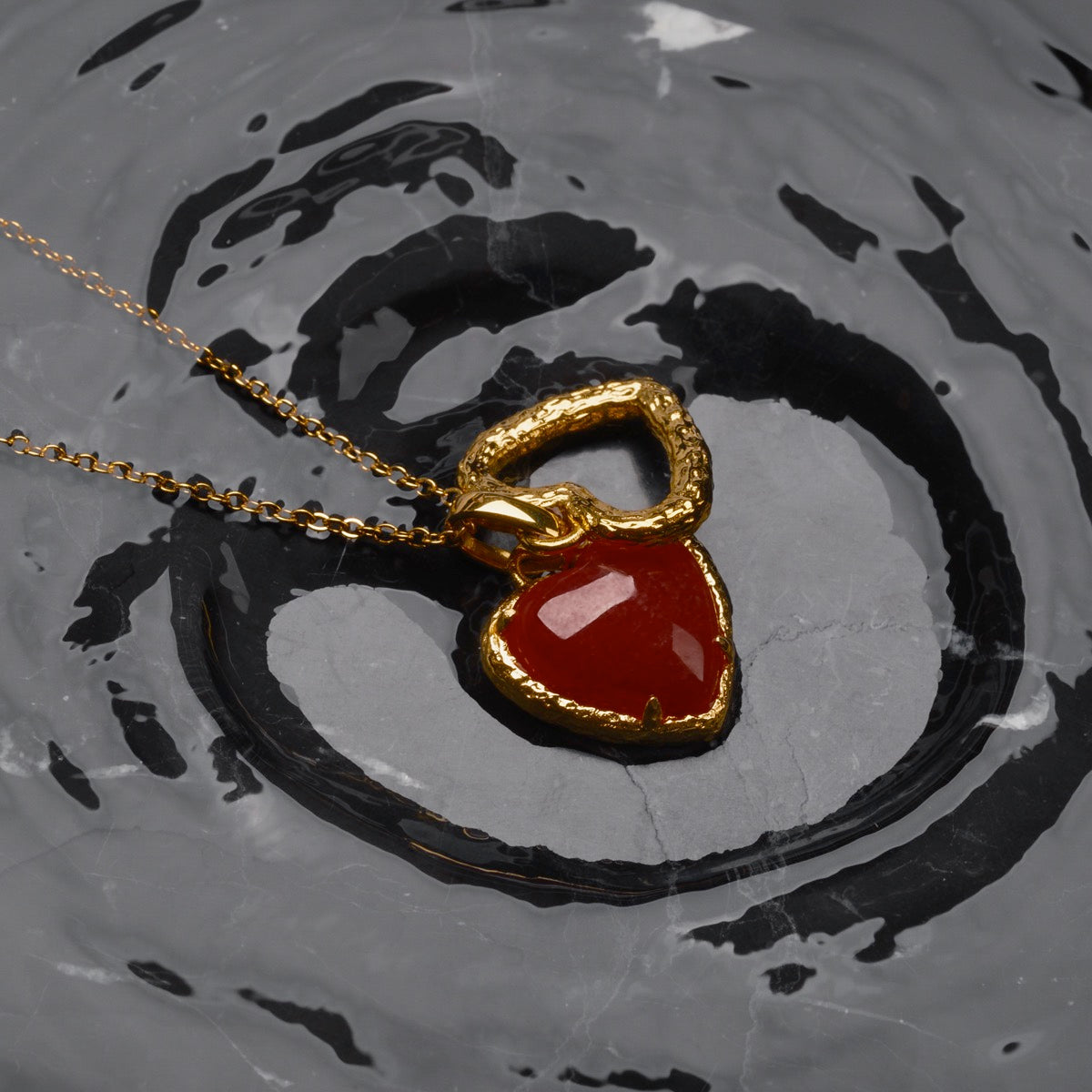 "Amorance Necklace", a gold chalcedony heart necklace with a textured finish on a reflective surface.