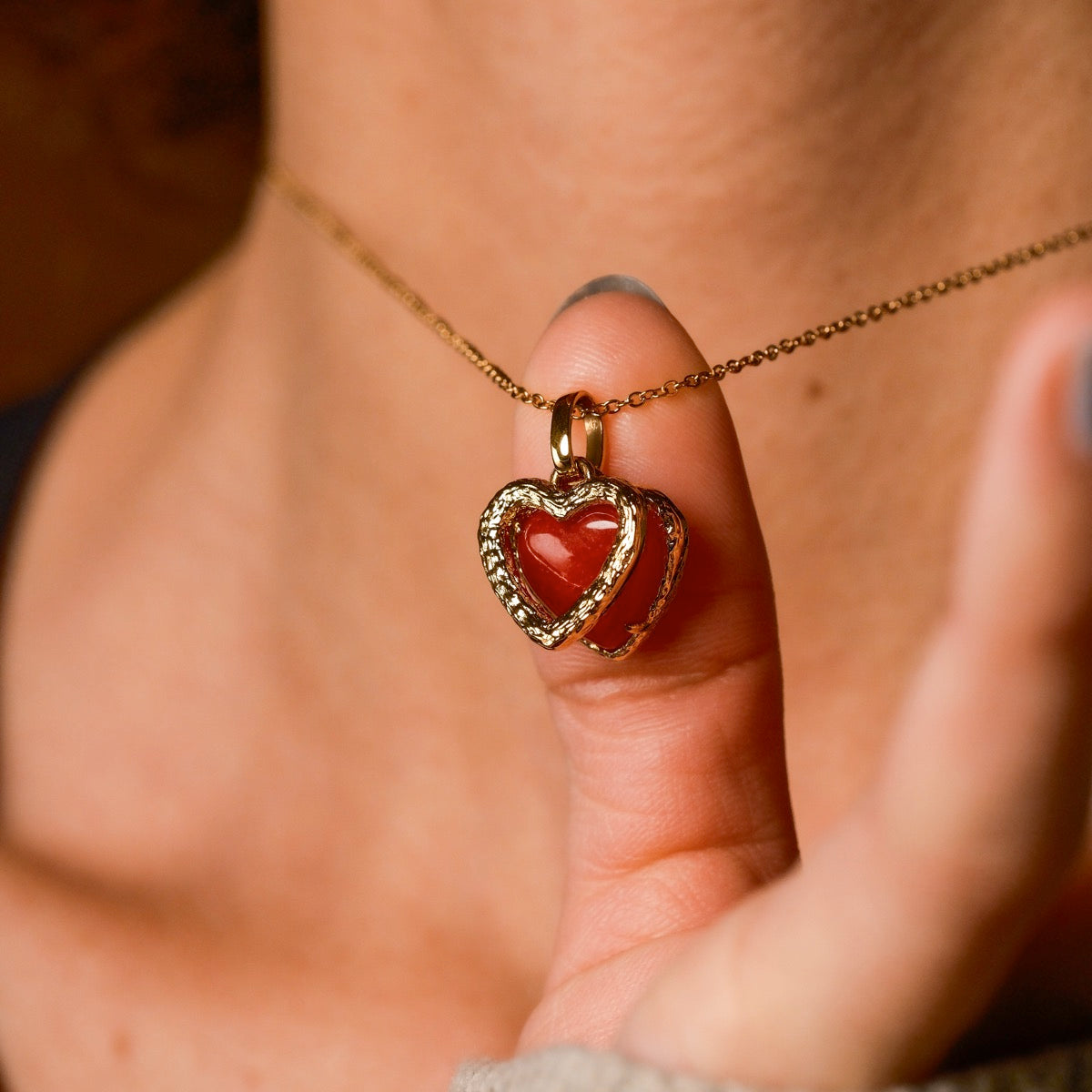 "Amorance Necklace": a heart-shaped pendant necklace with red chalcedony and gold accents, worn elegantly.
