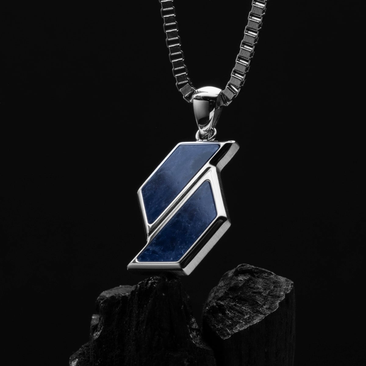 "Baritone Necklaces", a necklace with a modern geometric pendant in sodalite and silver, on a sleek chain against a dark background.