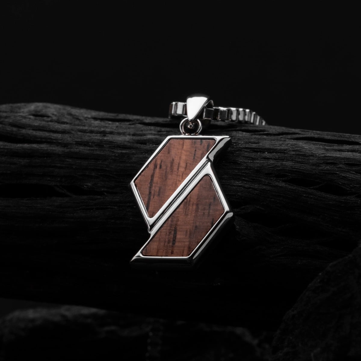 "Baritone Necklaces" necklace features a modern geometric design with walnut and silver accents against a dark backdrop.