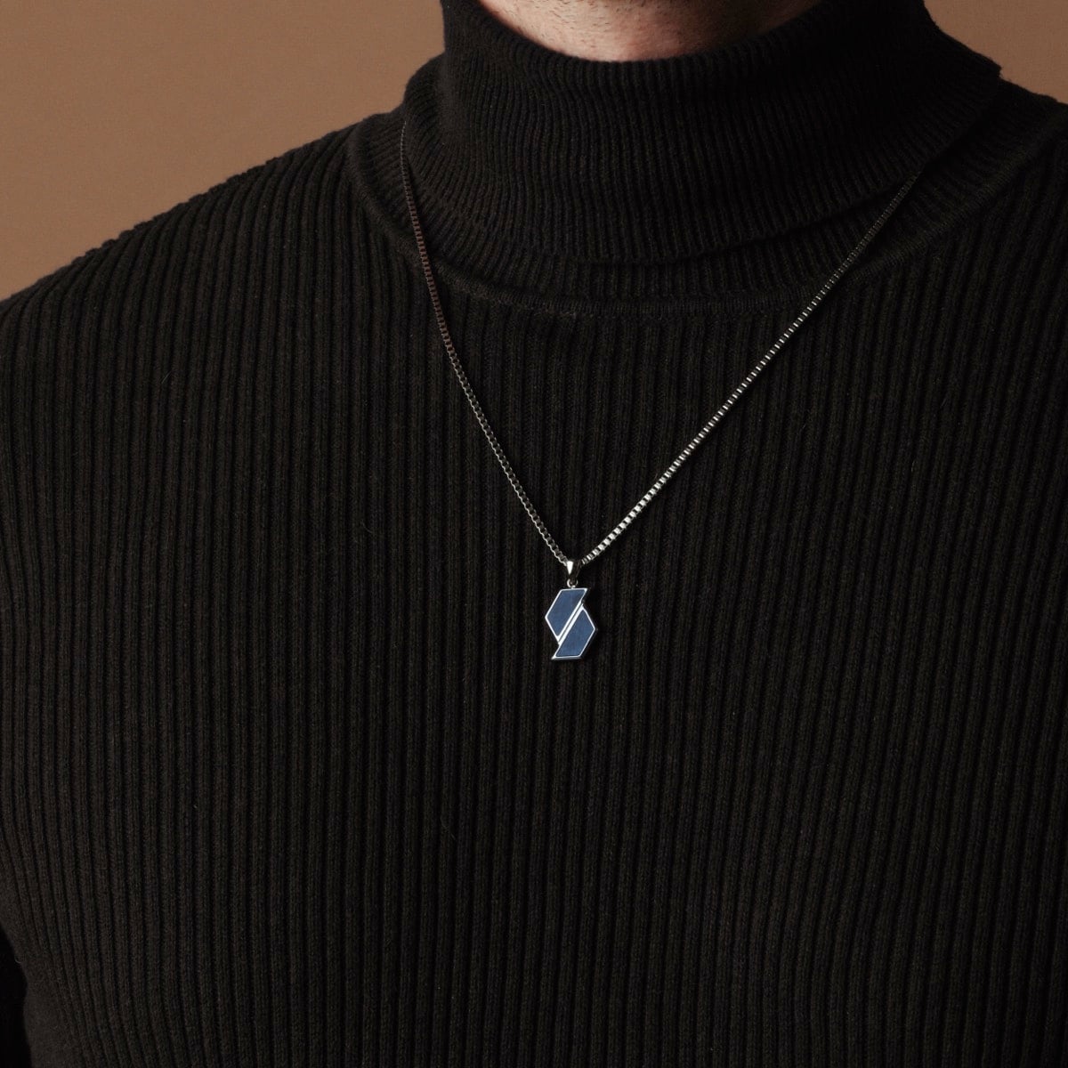 "Baritone Necklaces": Stylish silver necklace featuring a sodalite pendant on a ribbed black turtleneck background.