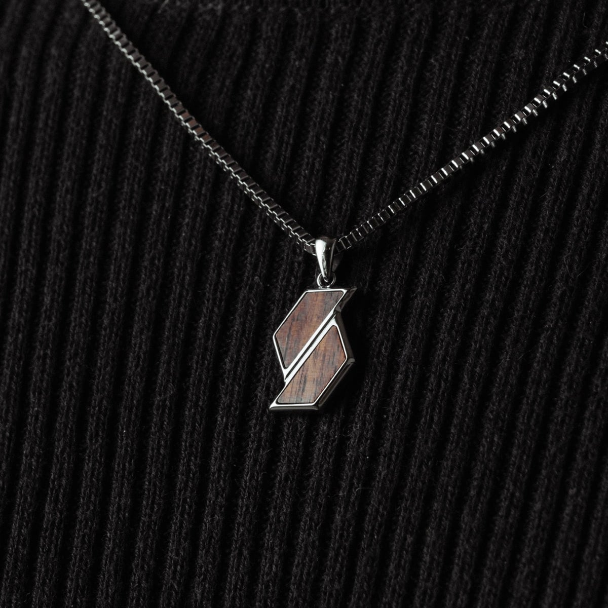 "Baritone Necklaces" necklace featuring a modern pendant design in Walnut and silver on a textured black background.