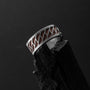 "Baritone Rings", a walnut and silver ring, features a geometric pattern with a bold, modern design against a dark background.