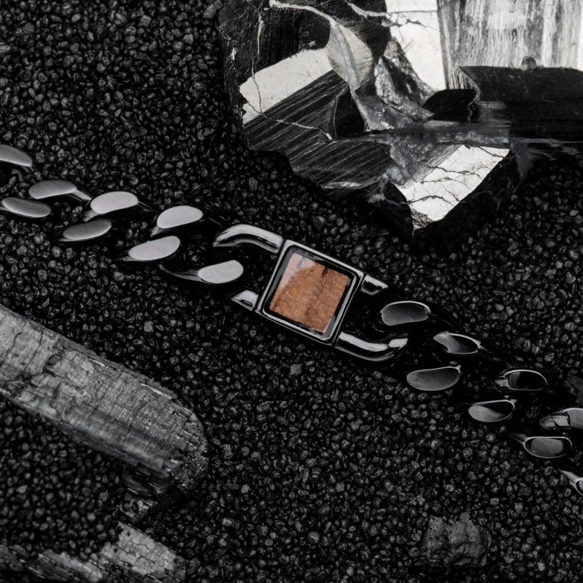 "Bodyguards Strap", a stylish black chain bracelet with a walnut accent, on a textured dark gray background.