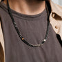 "Bodyguards Necklaces", a stylish necklace in walnut and dark gray tones, worn casually over a shirt.