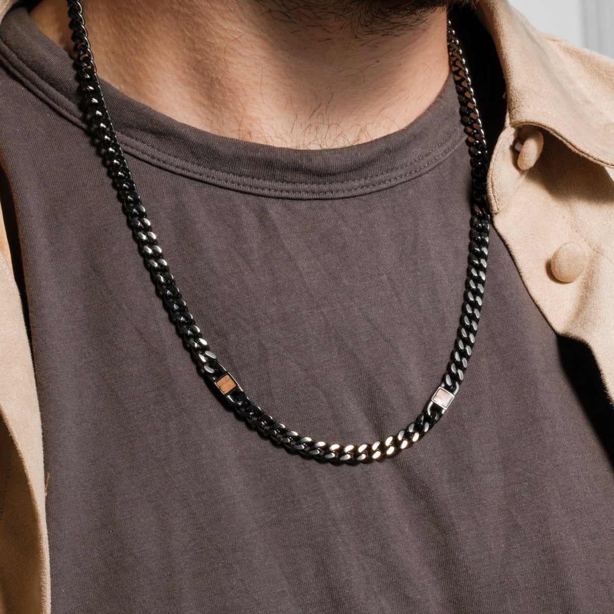 "Bodyguards Necklaces", a stylish necklace in walnut and dark gray tones, worn casually over a shirt.