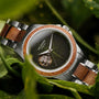 "Whisperwood" watch with a green leaf-patterned dial and koa wood accents, surrounded by lush greenery.