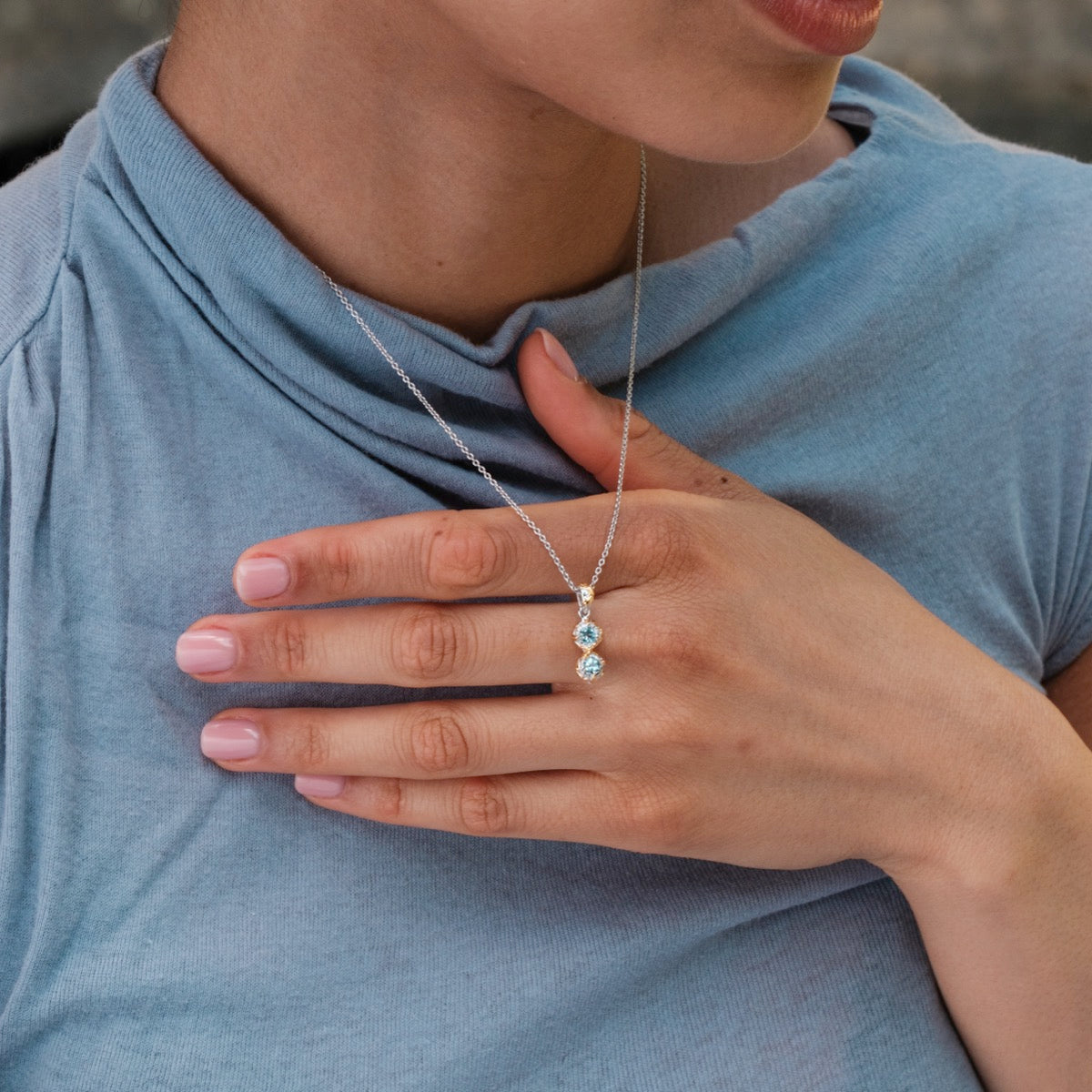 "Silverstream Necklace" necklace featuring a gold chain with topaz stones, elegantly worn against a soft blue top.