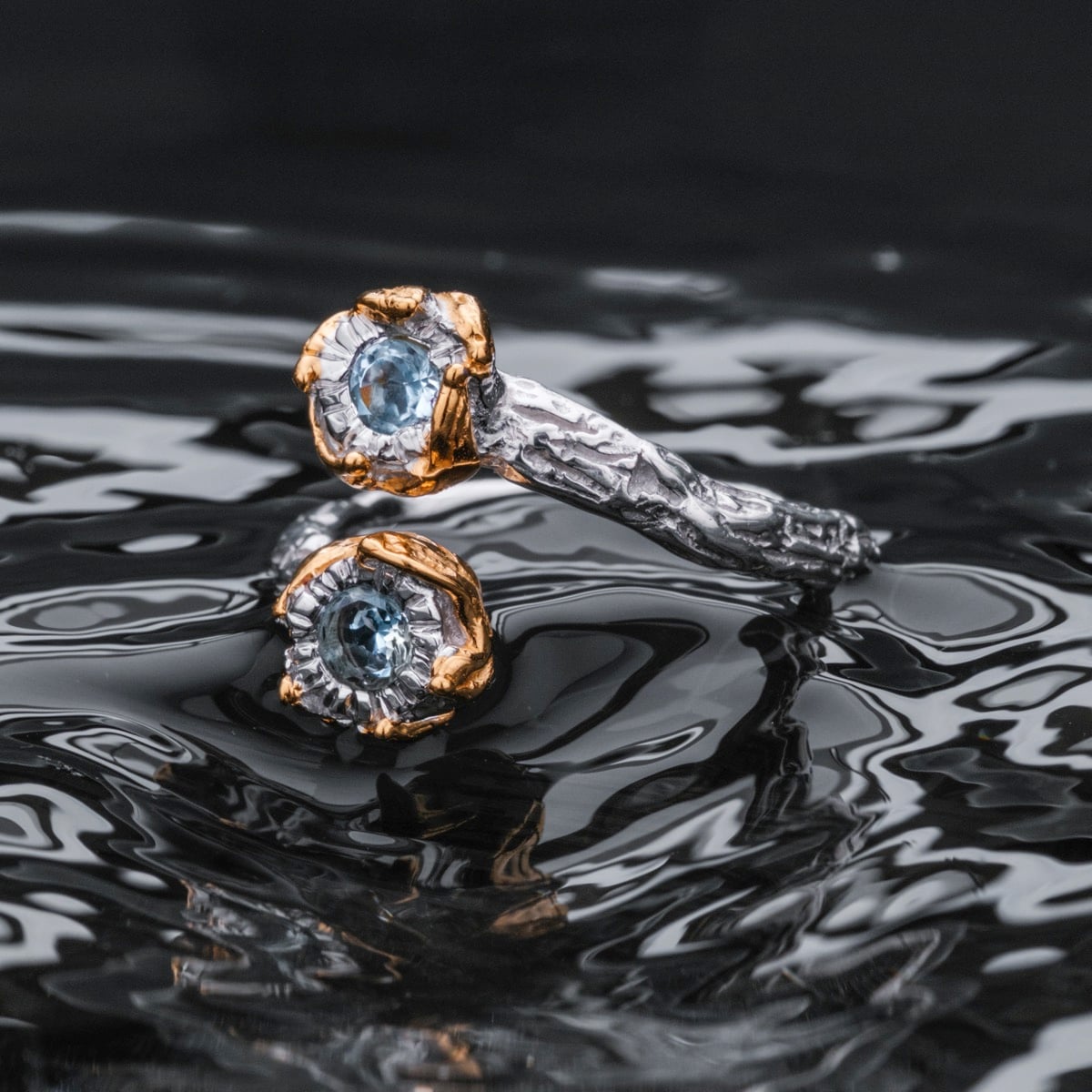 Silverstream Ring, an elegant ring featuring topaz and gold accents with a textured silver design against a reflective backdrop.