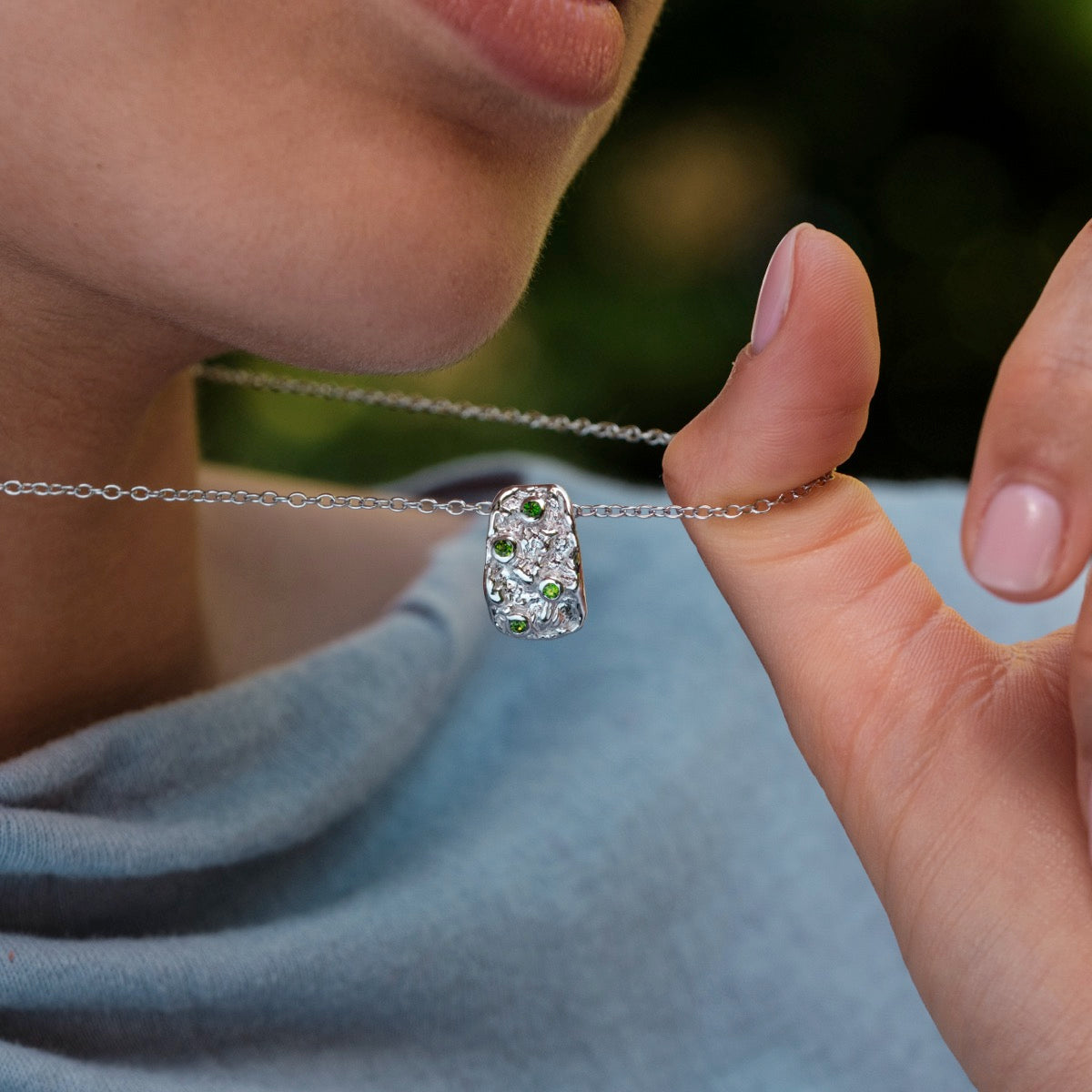 "Silverstream Necklace, elegant necklace featuring diopside stones on a delicate silver chain, held delicately by a woman wearing blue."