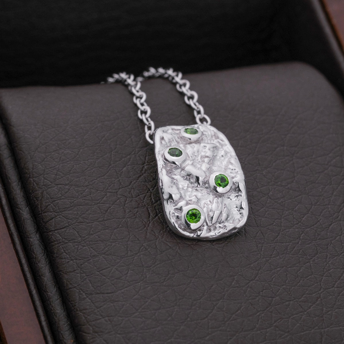 "Silverstream Necklace: A textured silver necklace adorned with green diopside stones."