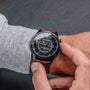 "Gmt Skywhirl" watch with marble and black dial, brown leather strap, worn on wrist.