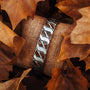 "Baritone" bracelet in Walnut and silver with a natural, textured design shown among autumn leaves.