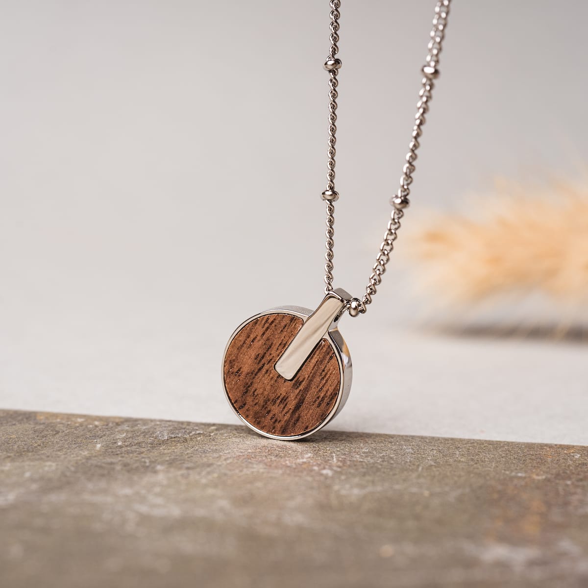 "Opacity Necklace": A stylish necklace featuring a walnut and silver circular pendant on a sleek chain.