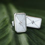 "Aquarell Earrings" earrings feature a modern geometric design with white nacre and silver accents on a leafy background.