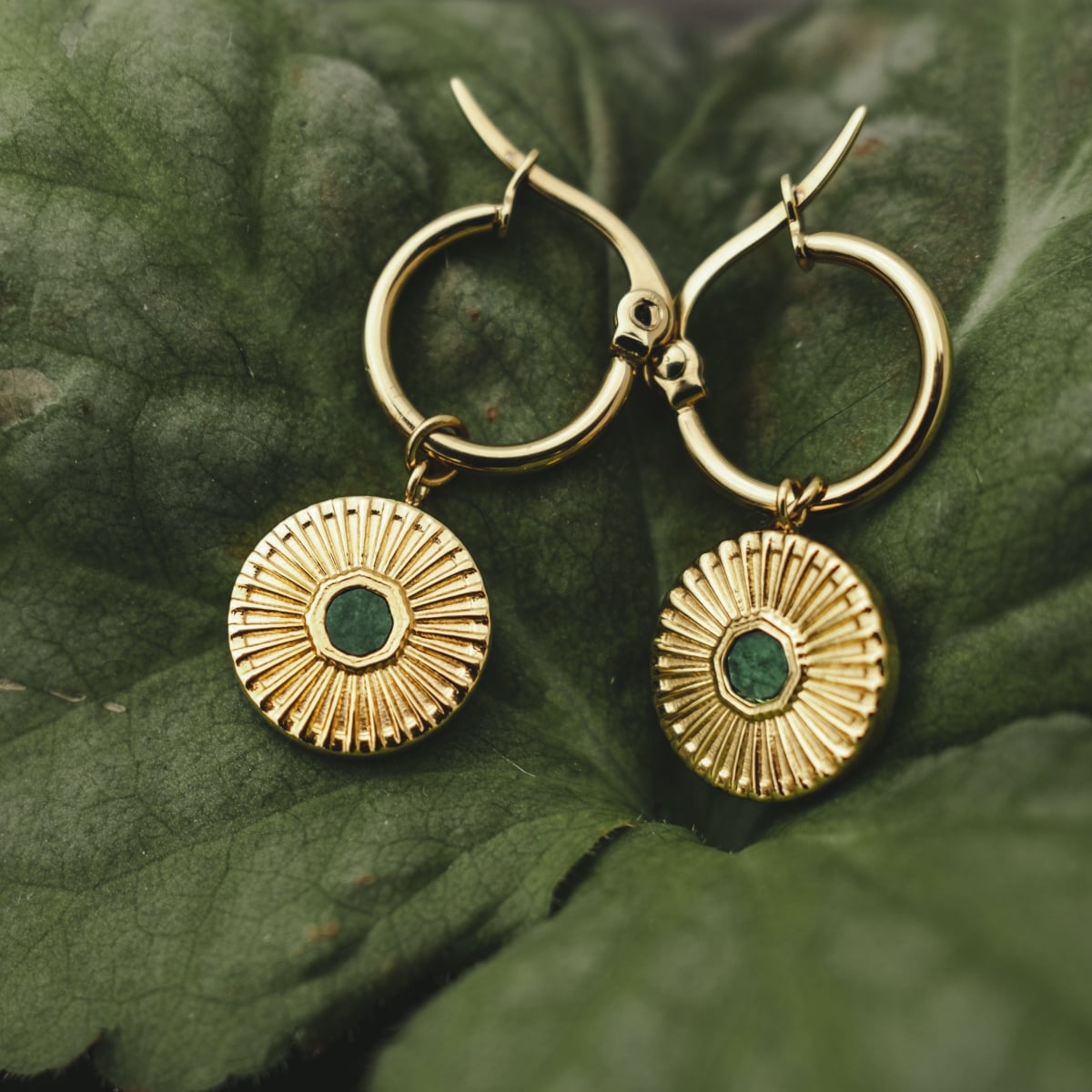 Stencil earrings, featuring a circular design with intricate marble and gold accents, resting on lush green leaves.