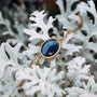 "Mirror Bracelet", an elegant bracelet featuring a Lapis Lazuli stone and gold chain, displayed on white decorative leaves.