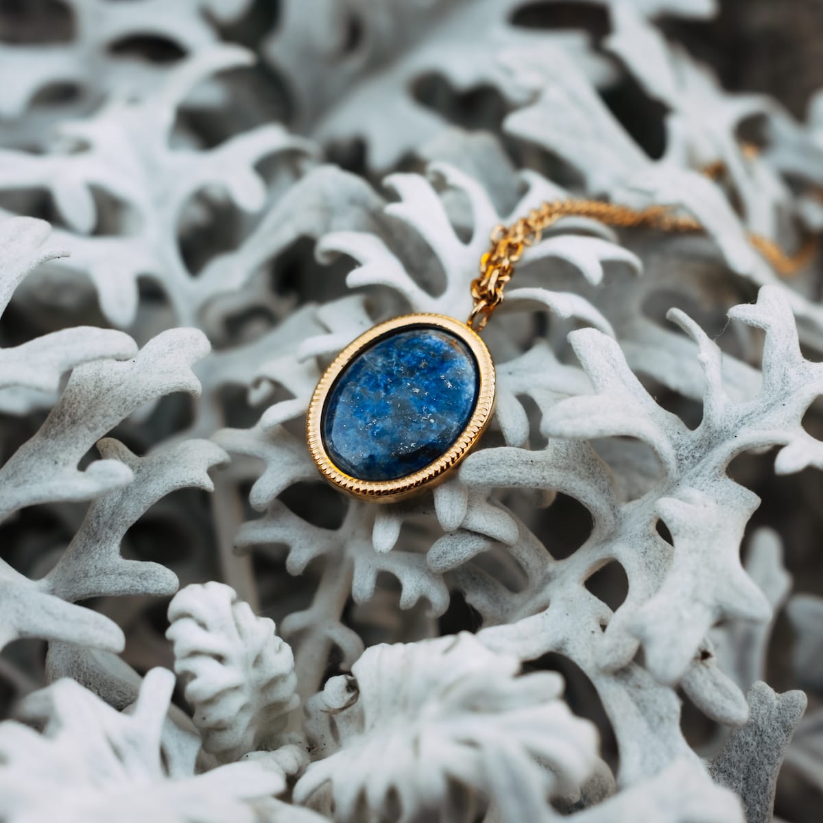 "Mirror Necklace" necklace in gold, featuring a lapis lazuli pendant set against a textured white background.