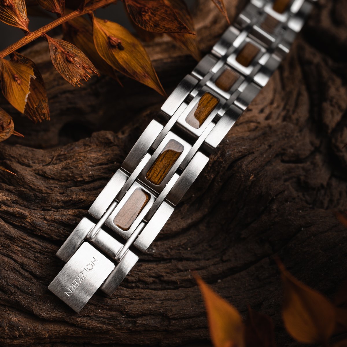 "Tremolo" watch bracelet features a sleek walnut and silver design, elegantly styled on a rustic wooden backdrop.