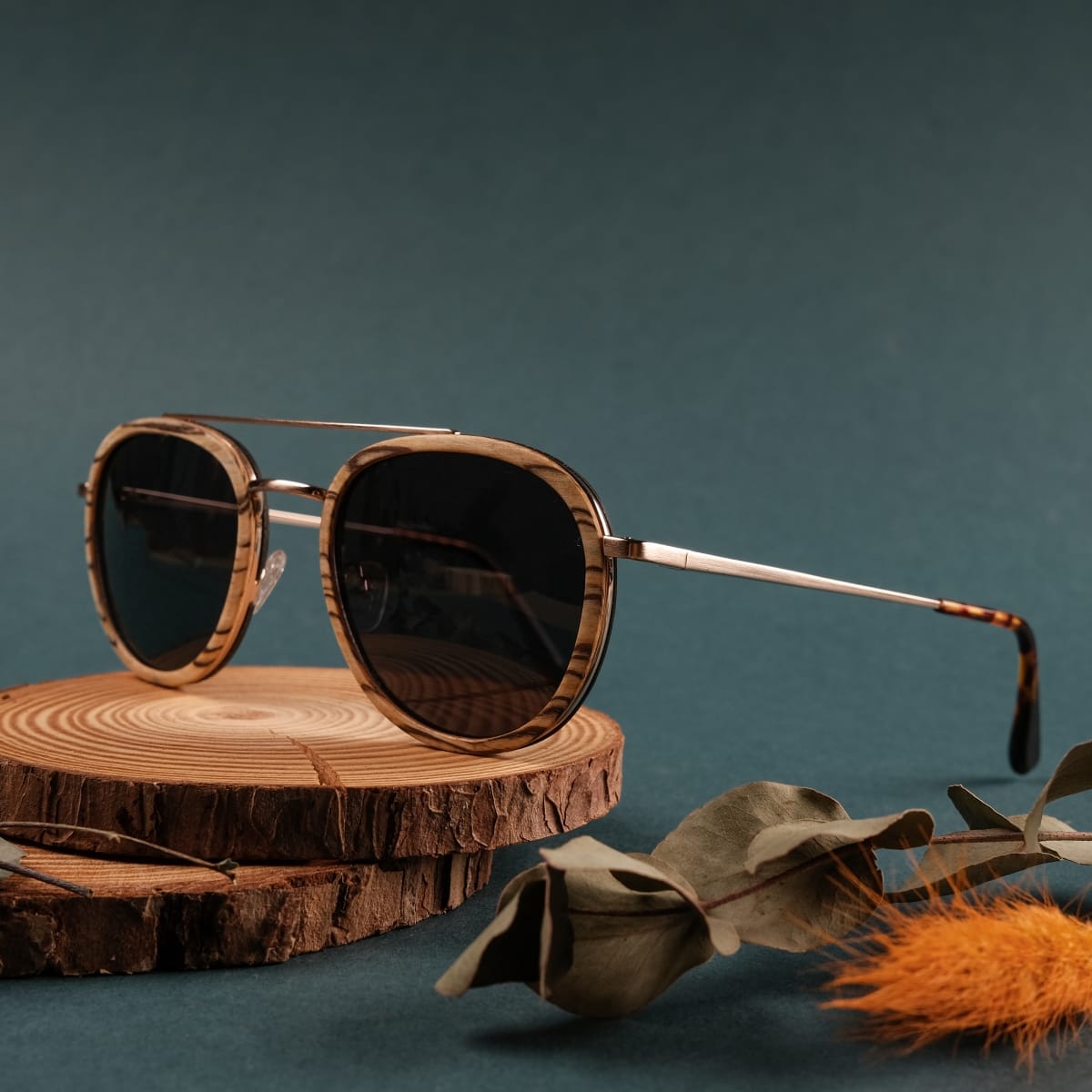 "The Risky" sunglasses with zebrawood frames and matte gold accents, showcased on a rustic wooden surface.