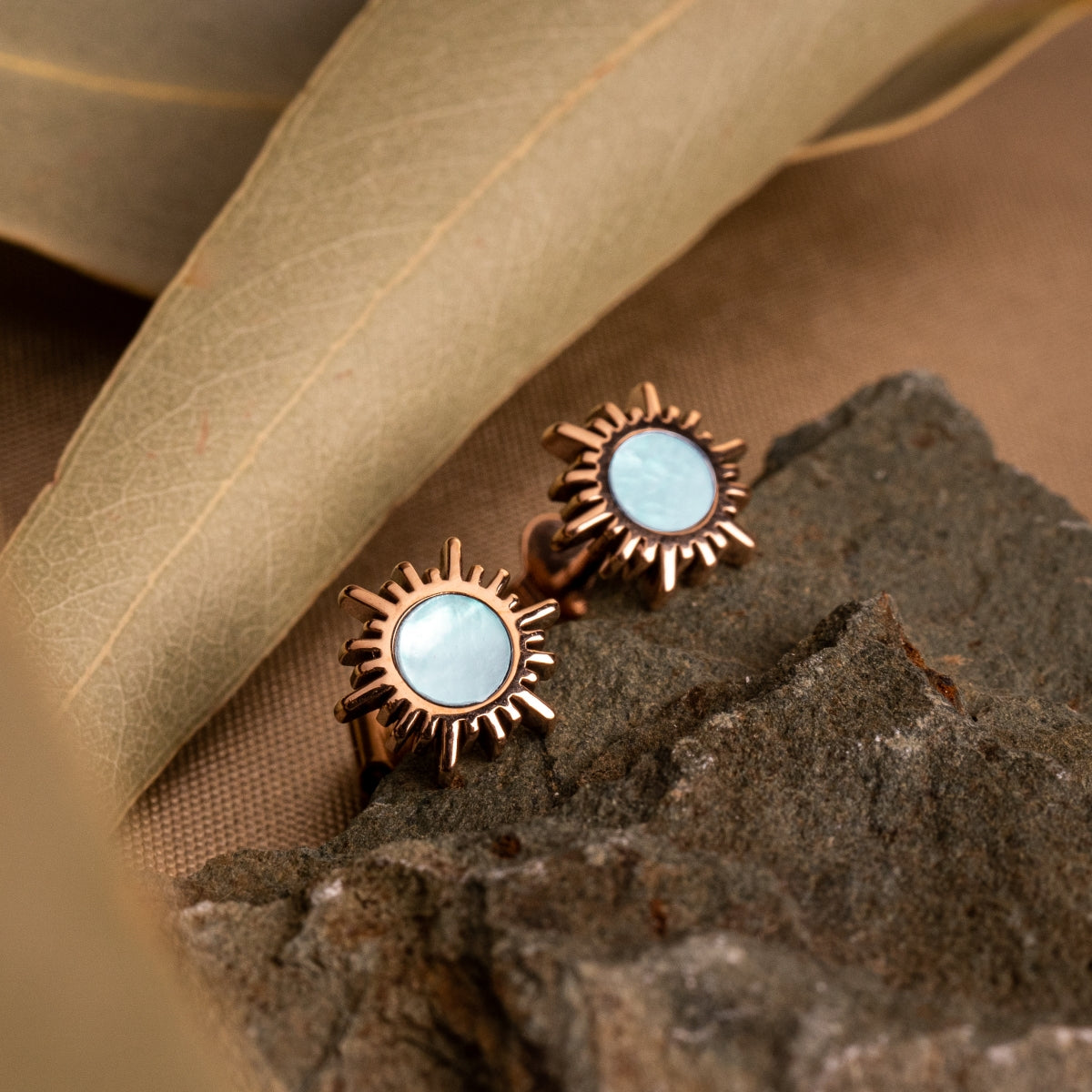 Shade Earrings: Elegant earrings in rose gold with a sunburst design and blue nacre center.