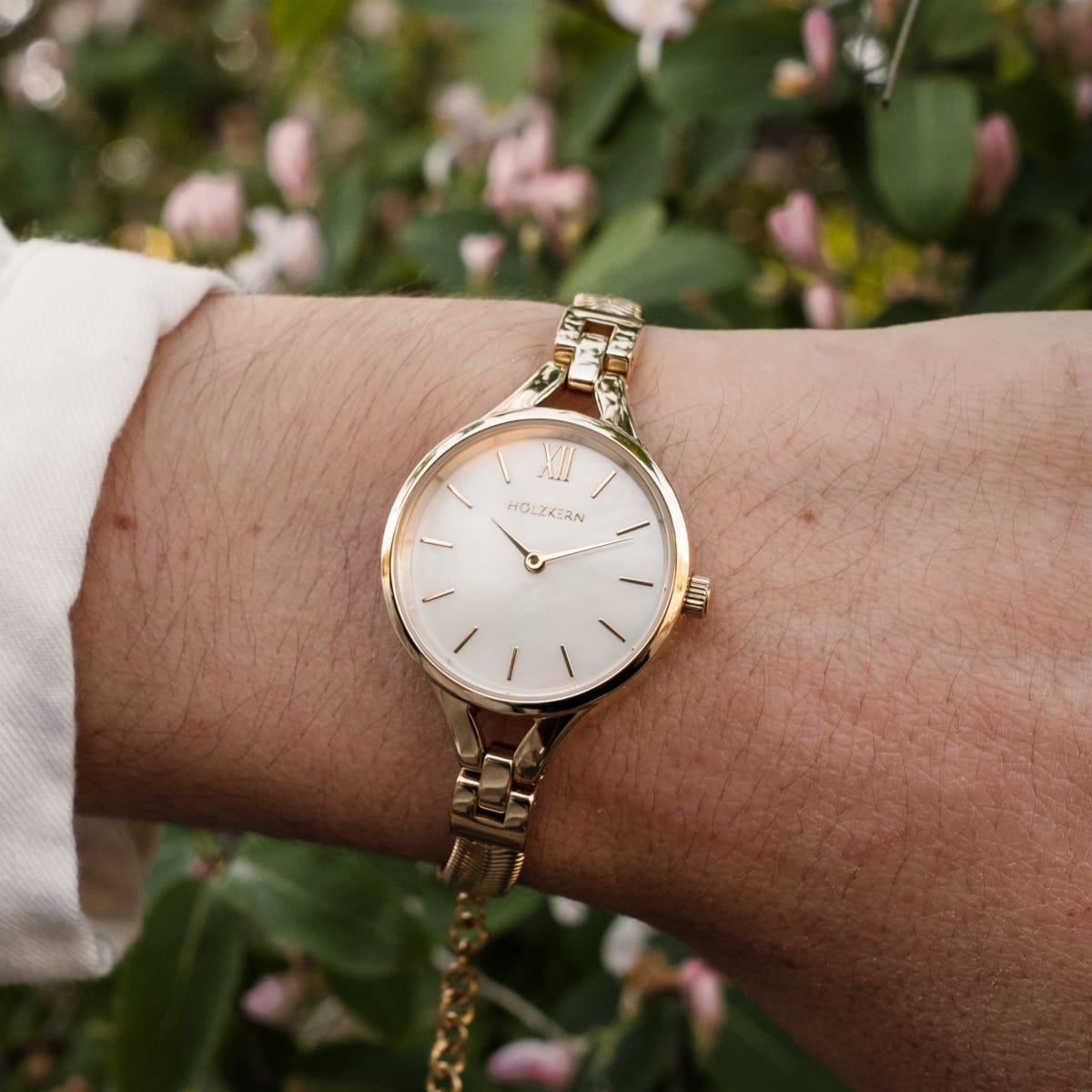 Elegant "Kaliya" watch with a nacre face and gold-tone bracelet, set against a floral backdrop.