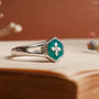 "Spectral Ring" - A silver and nacre ring featuring a hexagonal green gem with a star design, set against a warm background.