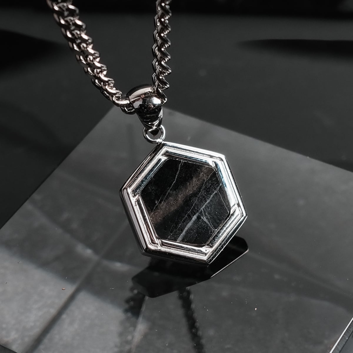 "Axis Necklace", a hexagonal necklace with a marble inset, framed in polished silver on a sleek chain.