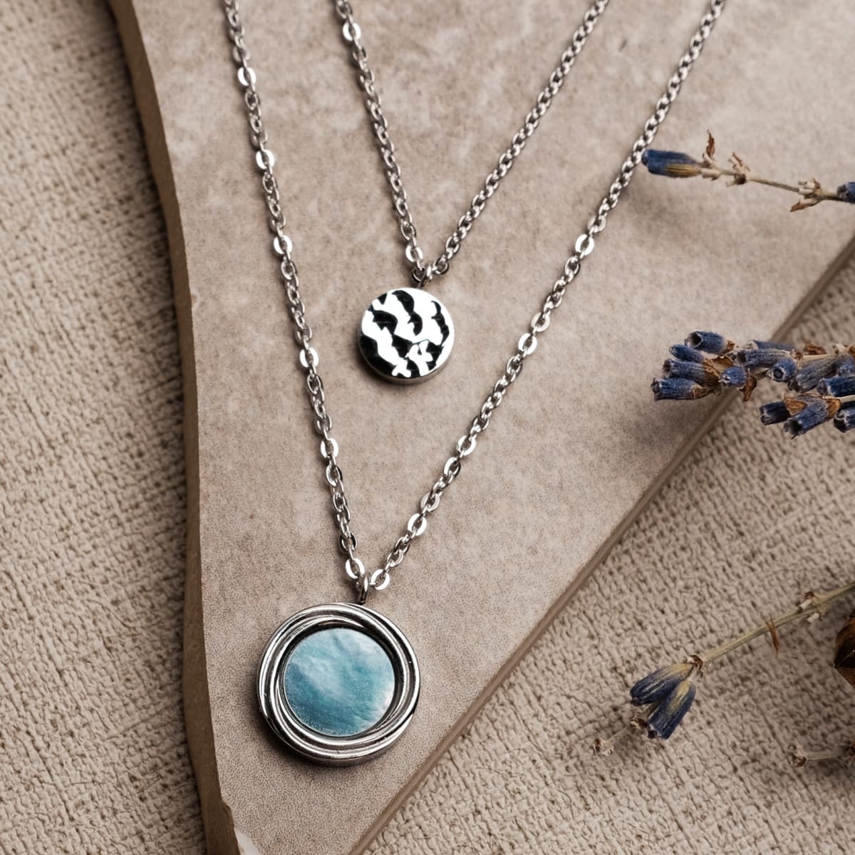 "Zendala Necklace" necklace in nacre and silver, featuring layered pendants on a textured background with dried lavender accents.