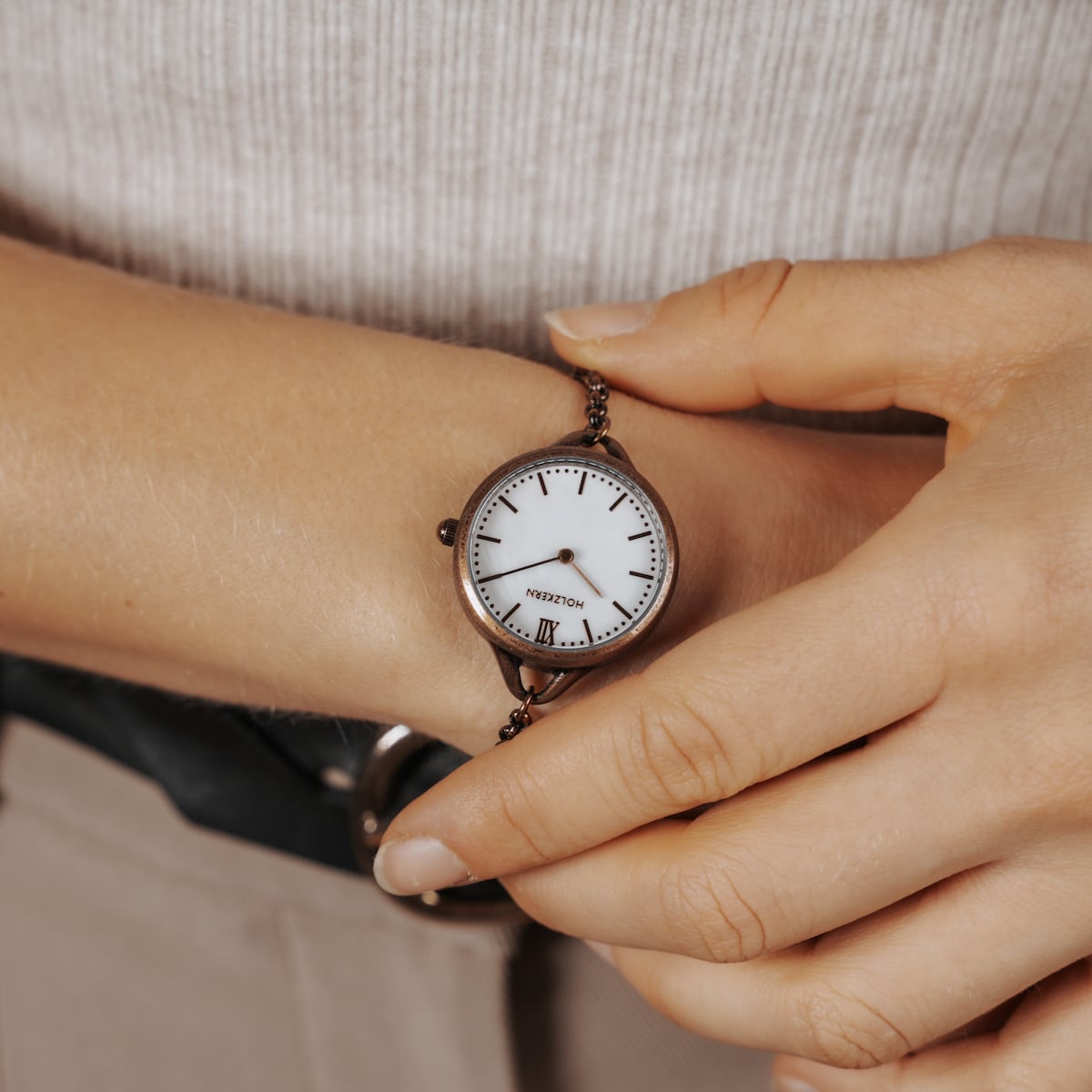 "Touching" watch featuring a nacre face and antique copper finish, worn on wrist for a classic look.