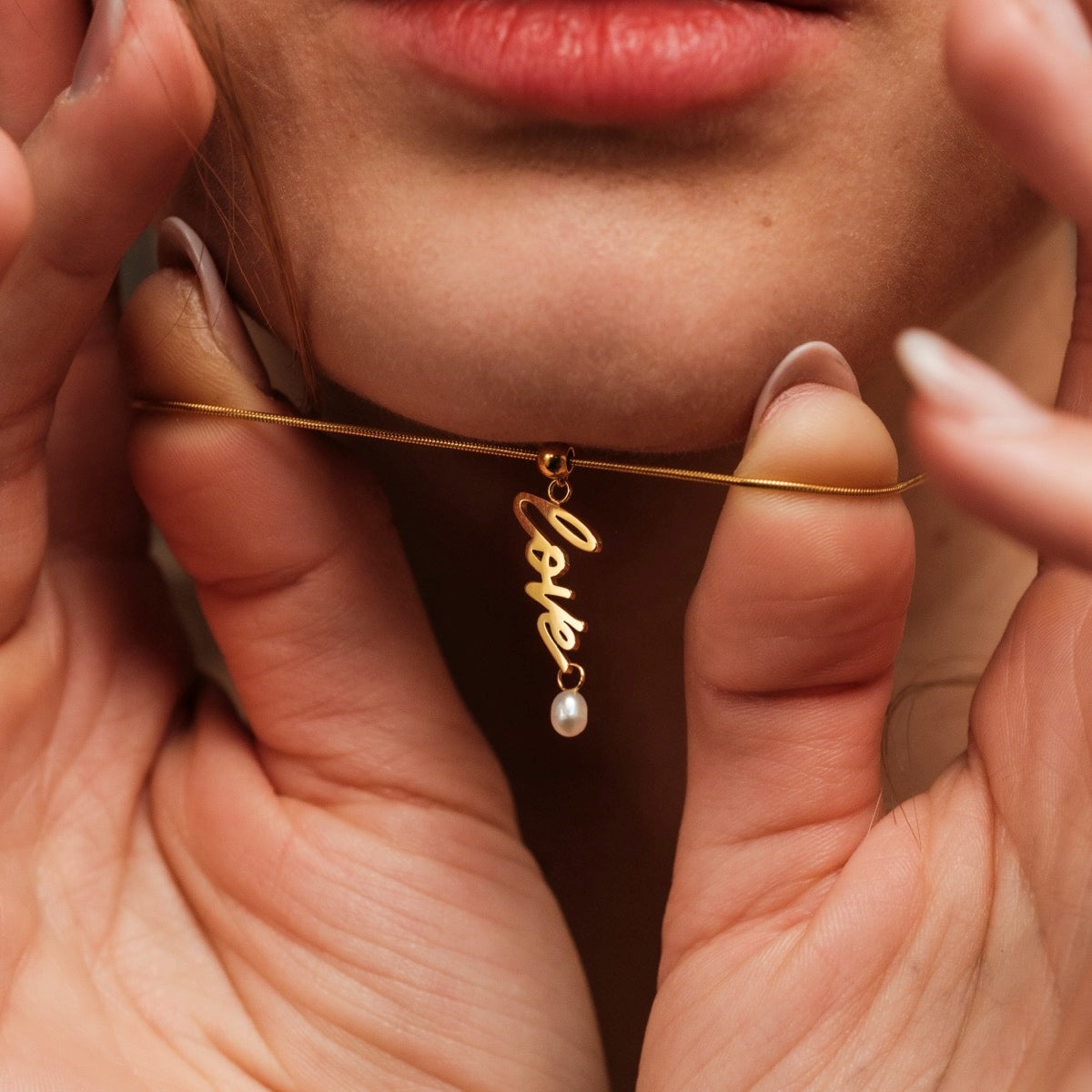 "Love-Charm", a gold and pearl necklace, elegantly styled with a script "love" charm.