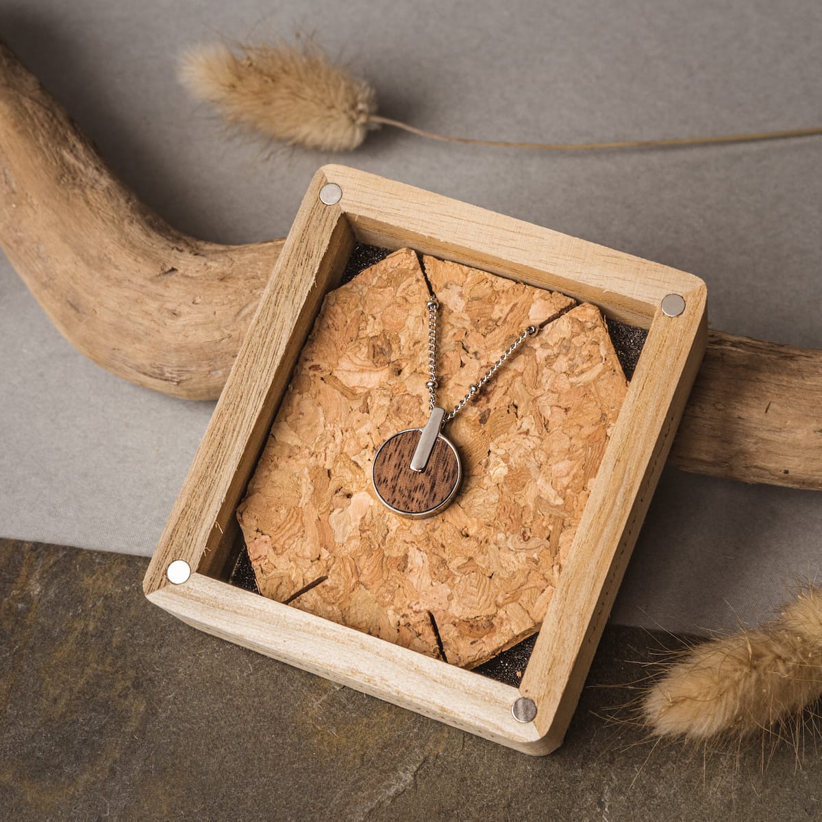 "Opacity Necklace", a walnut and silver necklace, showcased in a rustic wooden box.