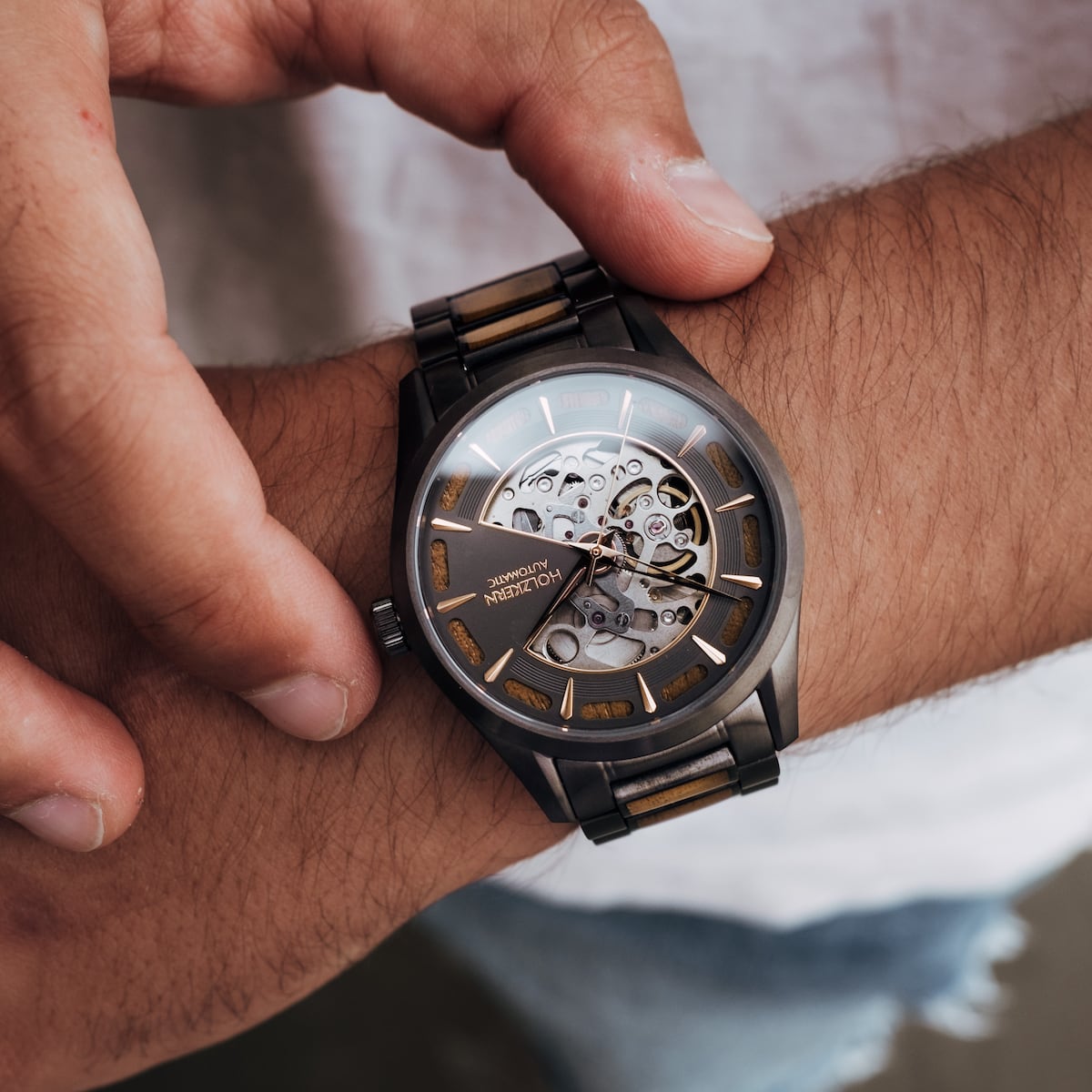 "Tenoumer" watch with a koa wood and dark gray design, featuring an open-face dial and metal wristband.